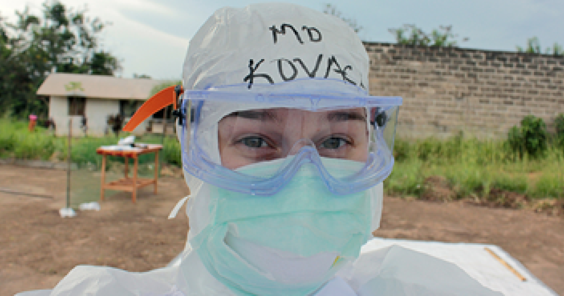 Doctor wearing a surgical mask, goggles, and scrub cap with "MD KOVACH" written on it