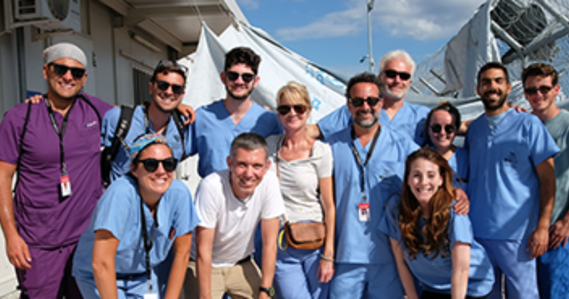 Group of 12 doctors wearing blue scrubs and smiling at camera