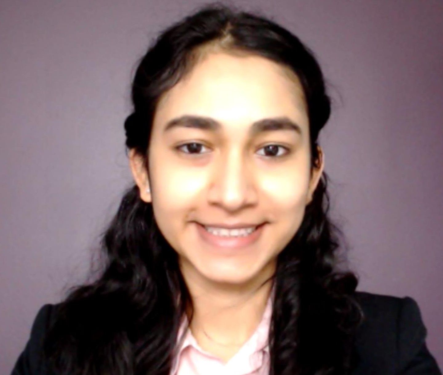 A woman smiling in a black shirt with a grey background.