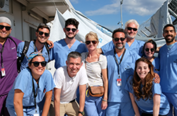 Group of 12 doctors wearing blue scrubs and smiling at camera